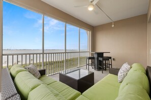 Ein Balkon mit einer Couch, einem Tisch und einer Bar, mit Blick auf einen Strand.