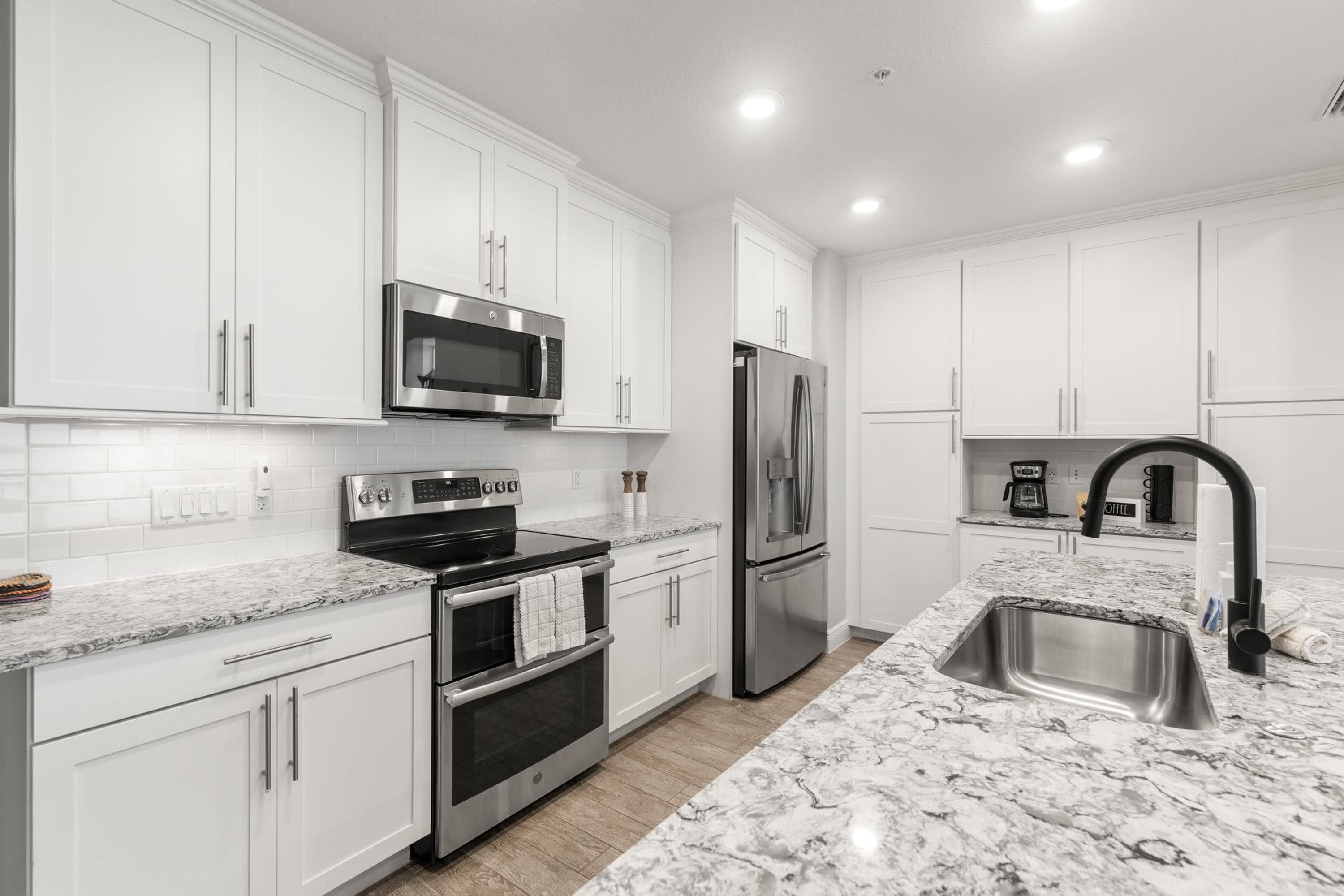 A modern kitchen with white cabinetry, stainless steel appliances, and a marble countertop.