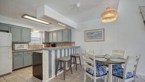 A kitchen with a built-in island, grey cabinets, and a dining area with white chairs and blue cushions. - Canal Views Pool 2 Min to Beach Fishing Pier (Corpus Christi)
