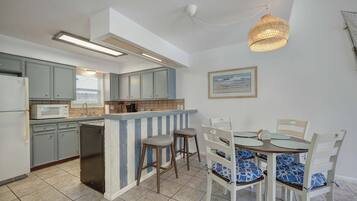 Een keuken met een inbouwkookeiland, grijze kastjes en een eethoek met witte stoelen en blauwe kussens.