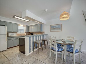 A kitchen with a built-in island, grey cabinets, and a dining area with white chairs and blue cushions. - Canal Views Pool 2 Min to Beach Fishing Pier (Corpus Christi)