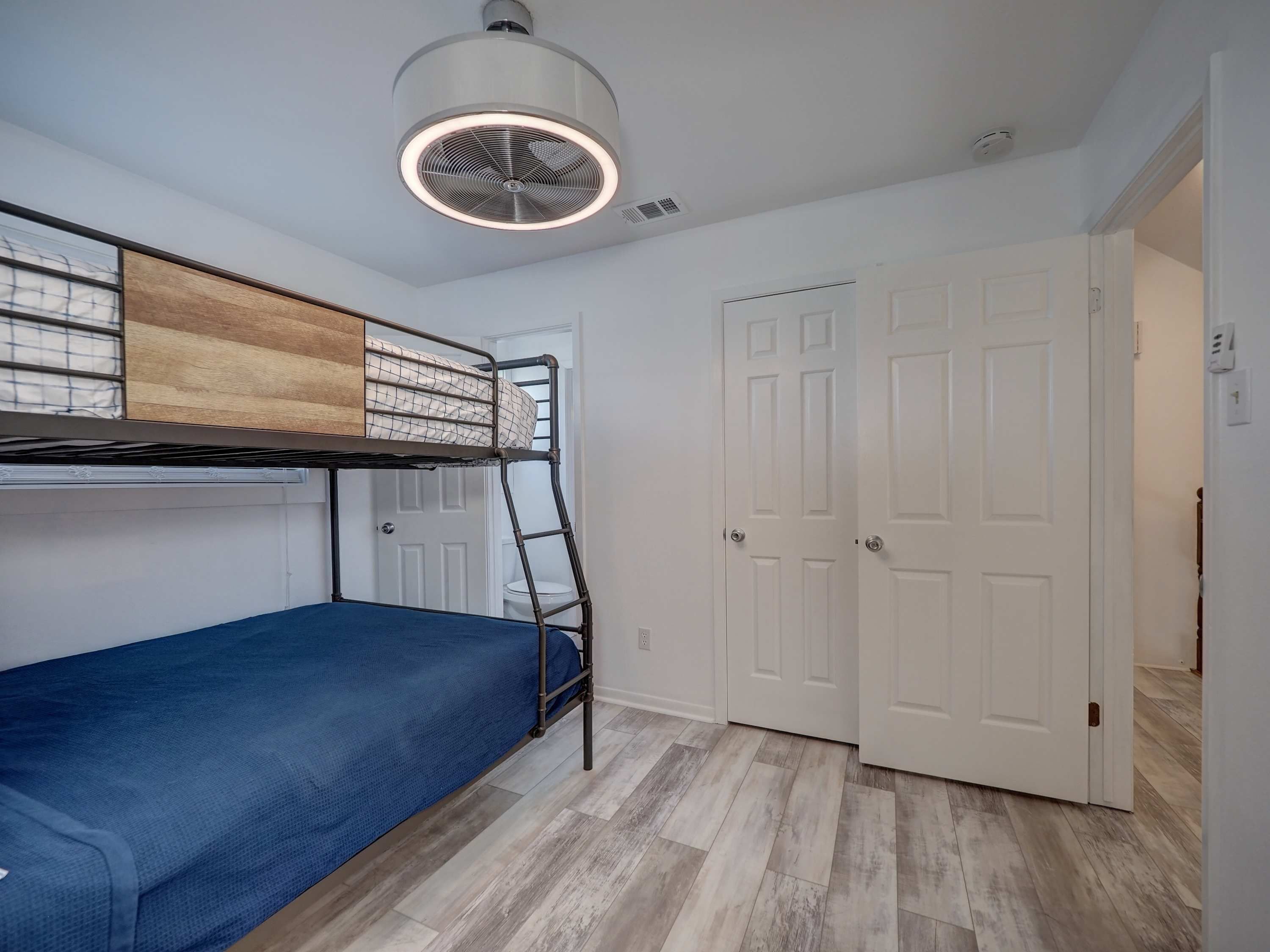 A bunk bed with a ladder, a ceiling fan, and white doors in a room with wooden flooring.