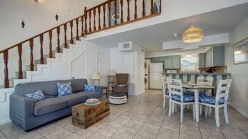 A spacious living area with a staircase, a dining table with chairs, and a kitchen area.