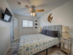 A bedroom with a bed, a ceiling fan, a window, wall art, a nightstand, and a lamp. - Canal Views Pool 2 Min to Beach Fishing Pier (Corpus Christi)