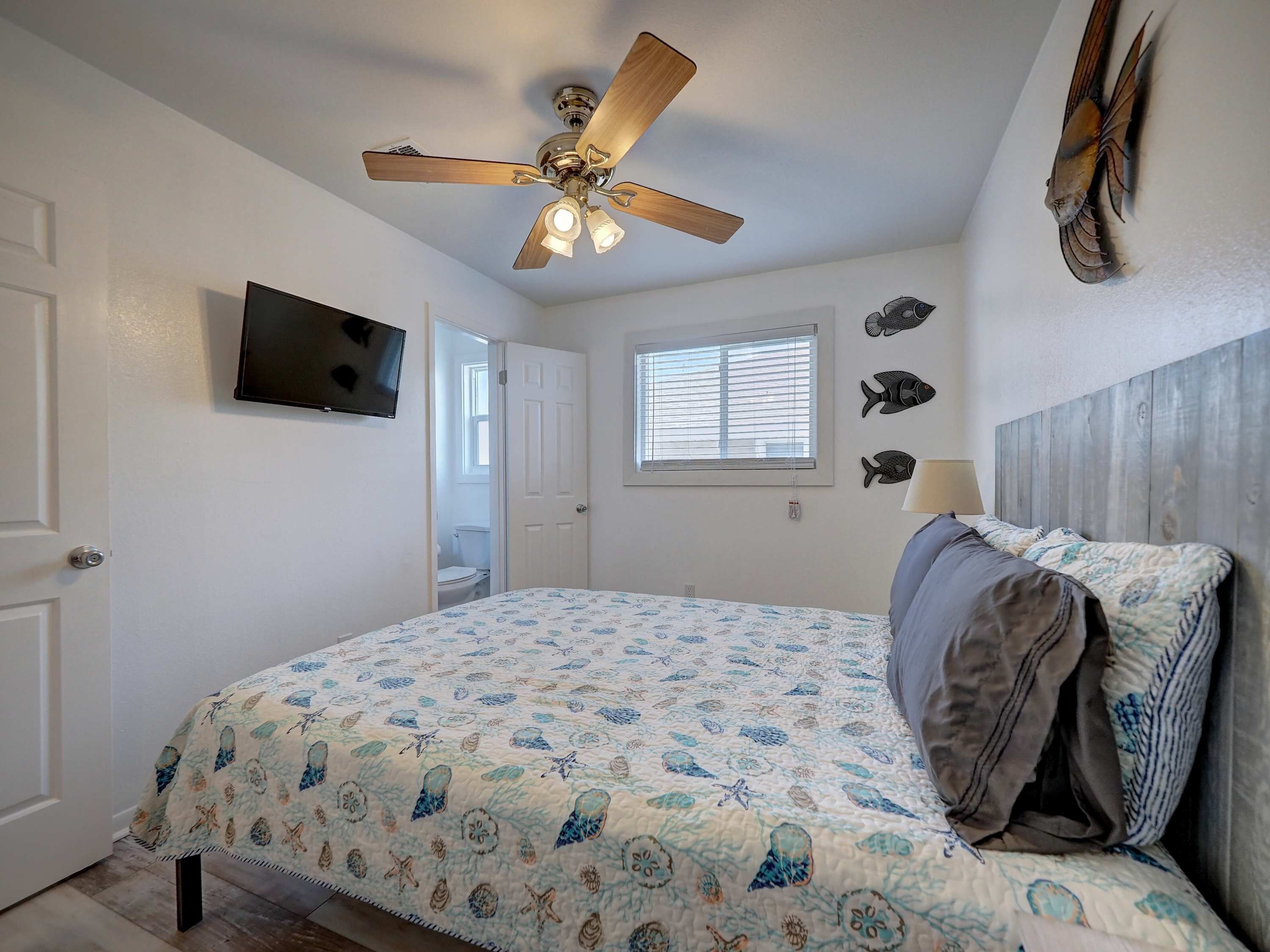 A bedroom with a bed, a ceiling fan, a TV, a window, and wall decorations.