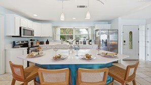 A modern kitchen with white cabinetry, a central island with chairs, and a large refrigerator. - Basketball Court Game Room Pool Hot Tub (Largo)