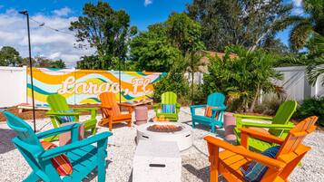 Un espacio al aire libre con sillas Adirondack de colores y un brasero.