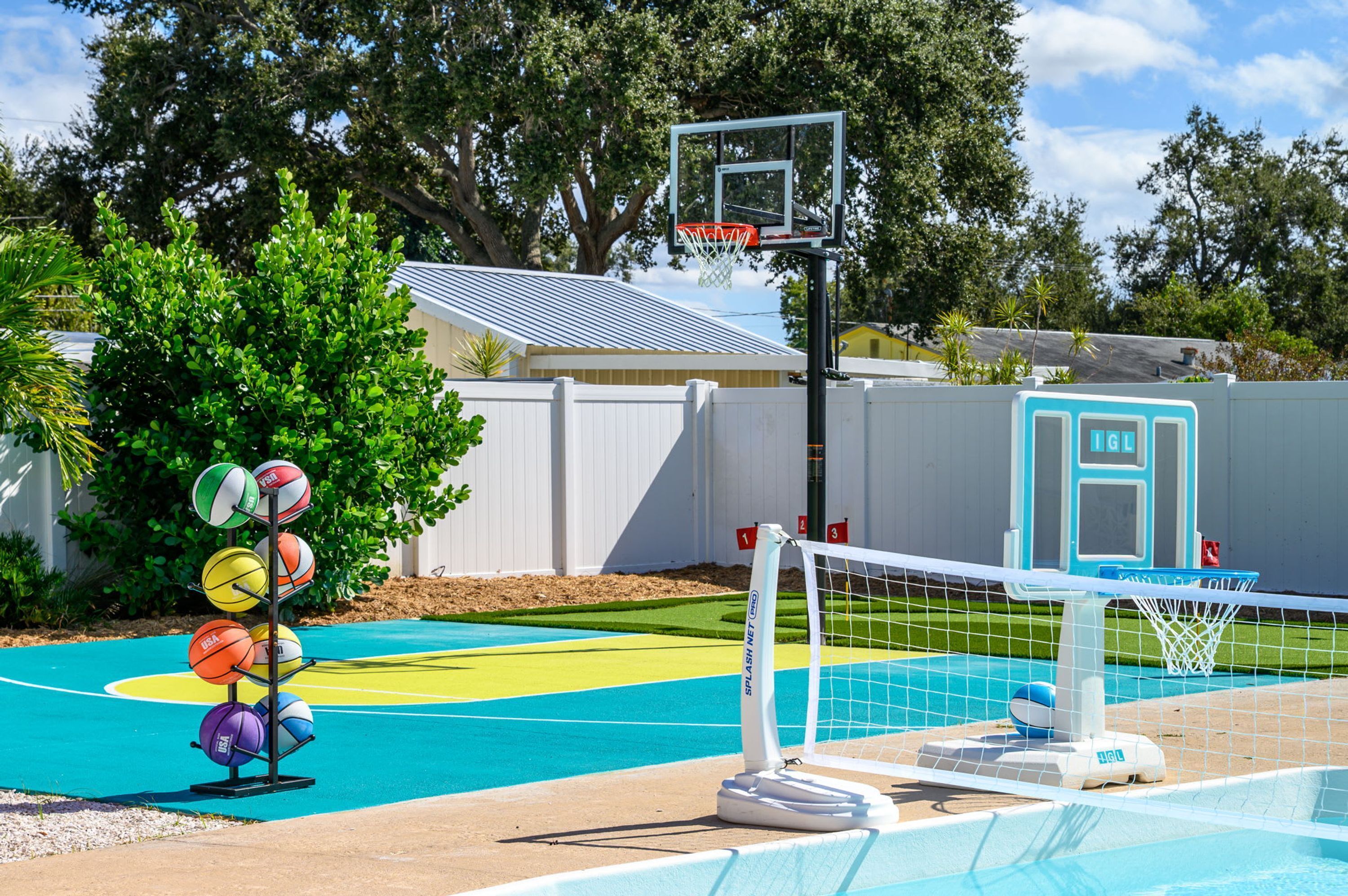 Una cancha de baloncesto junto a la piscina, con aro, red y un tendedero de balones.