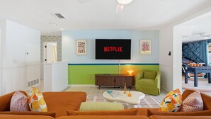 A living room with a flat-screen TV mounted on the wall, a ceiling fan, and a green armchair. - Basketball Court Game Room Pool Hot Tub (Largo)