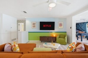 A living room with a flat-screen TV mounted on the wall, a ceiling fan, and a green armchair. - Basketball Court Game Room Pool Hot Tub (Largo)