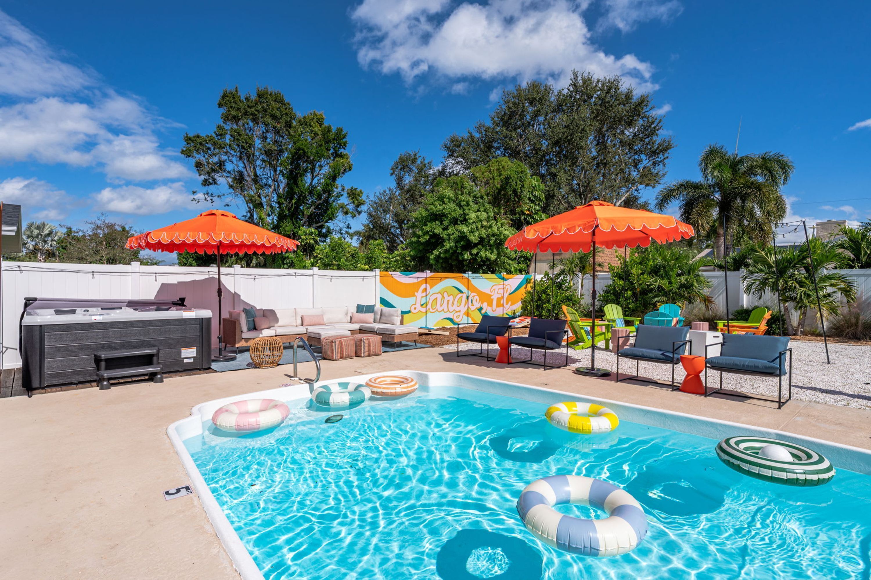 Una piscina con sillas de descanso y sombrillas, rodeada de follaje y un mural.