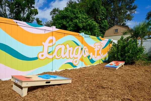A colorful mural with the text 'Largo, FL' on a fence, a wooden board game in the foreground, and a house in the background. - Basketball Court Game Room Pool Hot Tub (Largo)