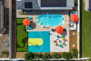 Vista aérea de una propiedad con piscina, cancha de tenis y zona ajardinada con sillas de descanso y sombrillas.