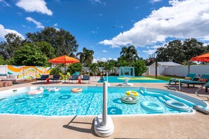 A swimming pool with lounge chairs and umbrellas, surrounded by trees and a colorful mural. - Basketball Court Game Room Pool Hot Tub (Largo)