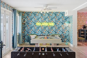 Una habitación con mesa de billar, mesa de fútbol de mesa y un letrero de neón que dice 'ON LARGO TIME'.