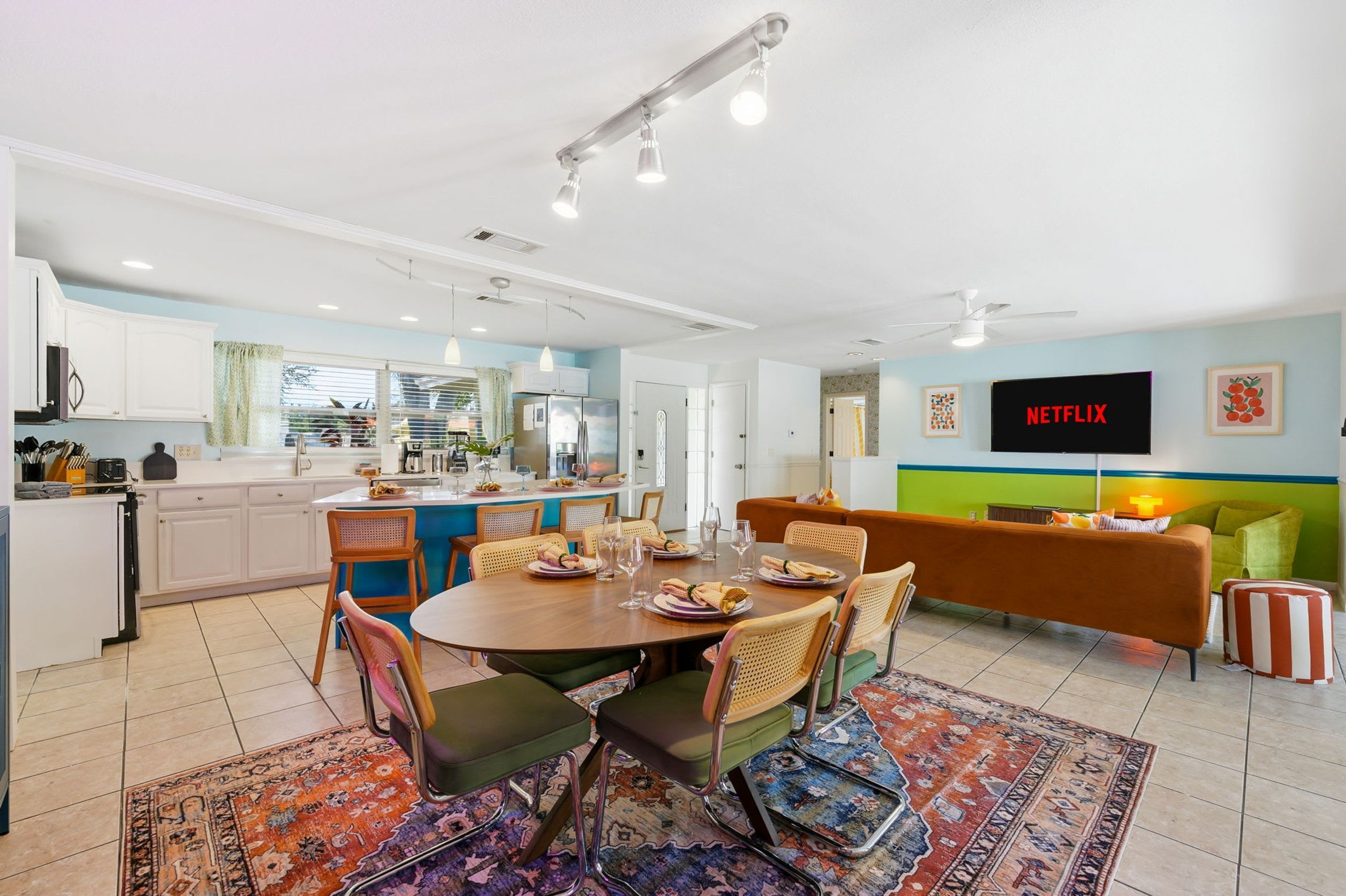 A modern living space with a dining area, kitchen, and a seating area with a TV displaying 'NETFLIX'.