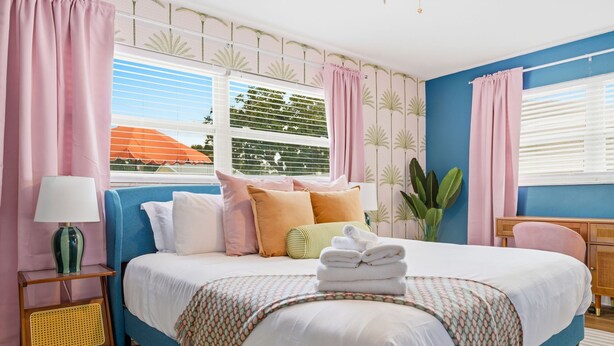 A bedroom with a bed, pillows, a bedside table, a lamp, and a window with curtains. - Basketball Court Game Room Pool Hot Tub (Largo)