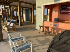 Een overdekt terras met houten stoelen en krukjes, een houten schommelset en een bar met krukjes en een kleine Amerikaanse vlag.