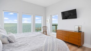 A bedroom with a large bed, a wooden dresser, and a TV on the wall. - Waterfront Getaway With Pier Access (Aransas Pass)