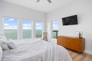 A bedroom with a large bed, a wooden dresser, and a TV on the wall.