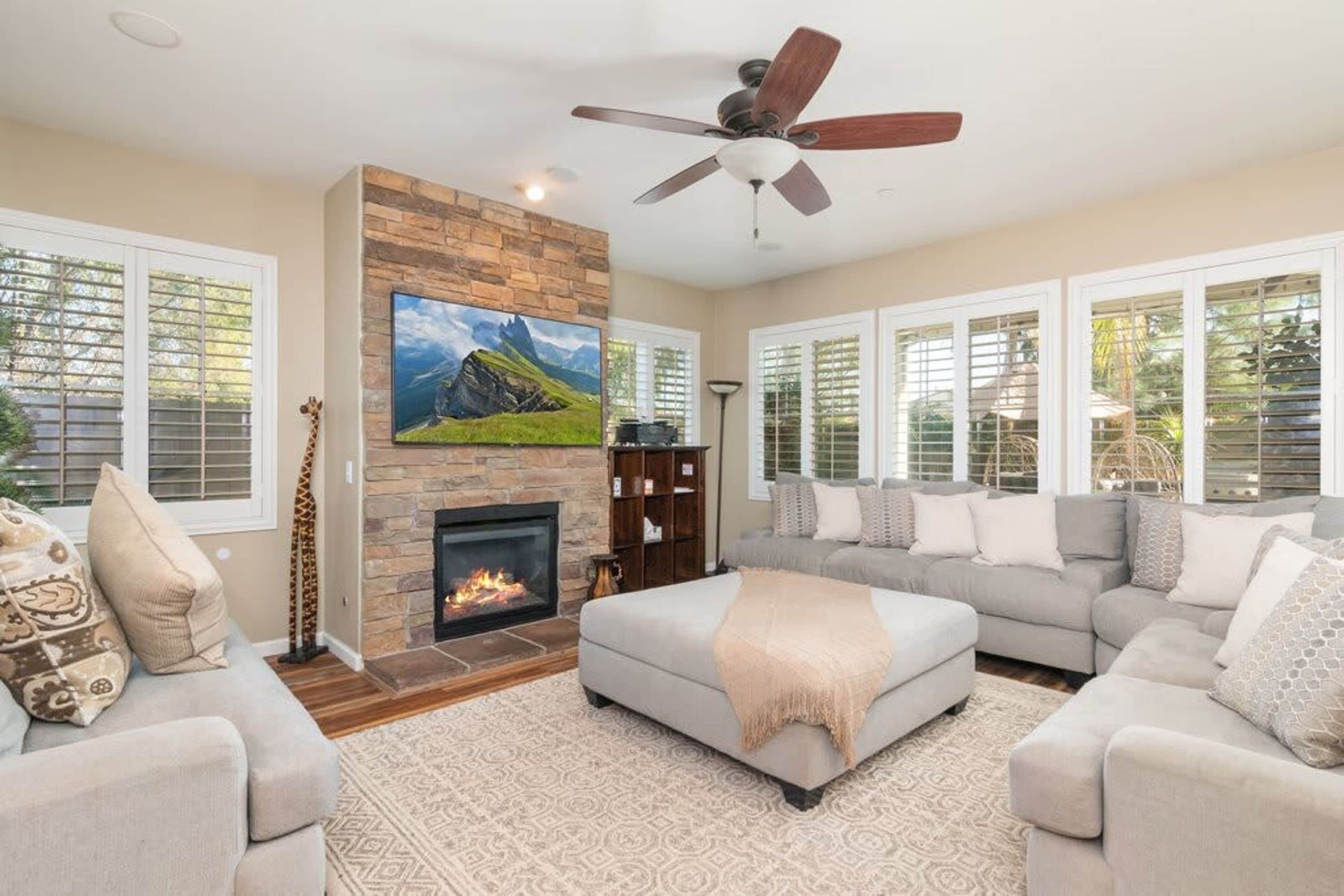 A living room with a fireplace, a ceiling fan, and a large TV mounted on a stone wall.