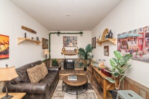 A cozy living room with a leather sofa, a coffee table, and a fireplace. There are wall-mounted shelves with decorative items and a large painting above the fireplace. - Minutes to Wineries Outdoor Oasis Pool Table (Murrieta)