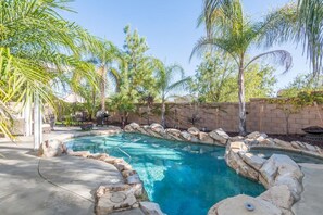 A backyard with a swimming pool surrounded by rocks and palm trees. - Minutes to Wineries Outdoor Oasis Pool Table (Murrieta)