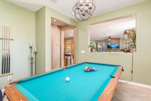A pool table with a white cue ball, surrounded by a teal playing surface, in a room with light green walls and a large mirror reflecting a kitchen area. - Minutes to Wineries Outdoor Oasis Pool Table (Murrieta)