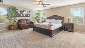 Ein Schlafzimmer mit einem großen Bett, einem Ledersofa, zwei Kübelpflanzen und einem Deckenventilator.