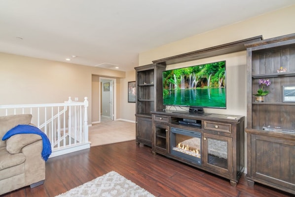 A living room with a flat-screen TV, wooden entertainment center, and a white railing. - Minutes to Wineries Outdoor Oasis Pool Table (Murrieta)
