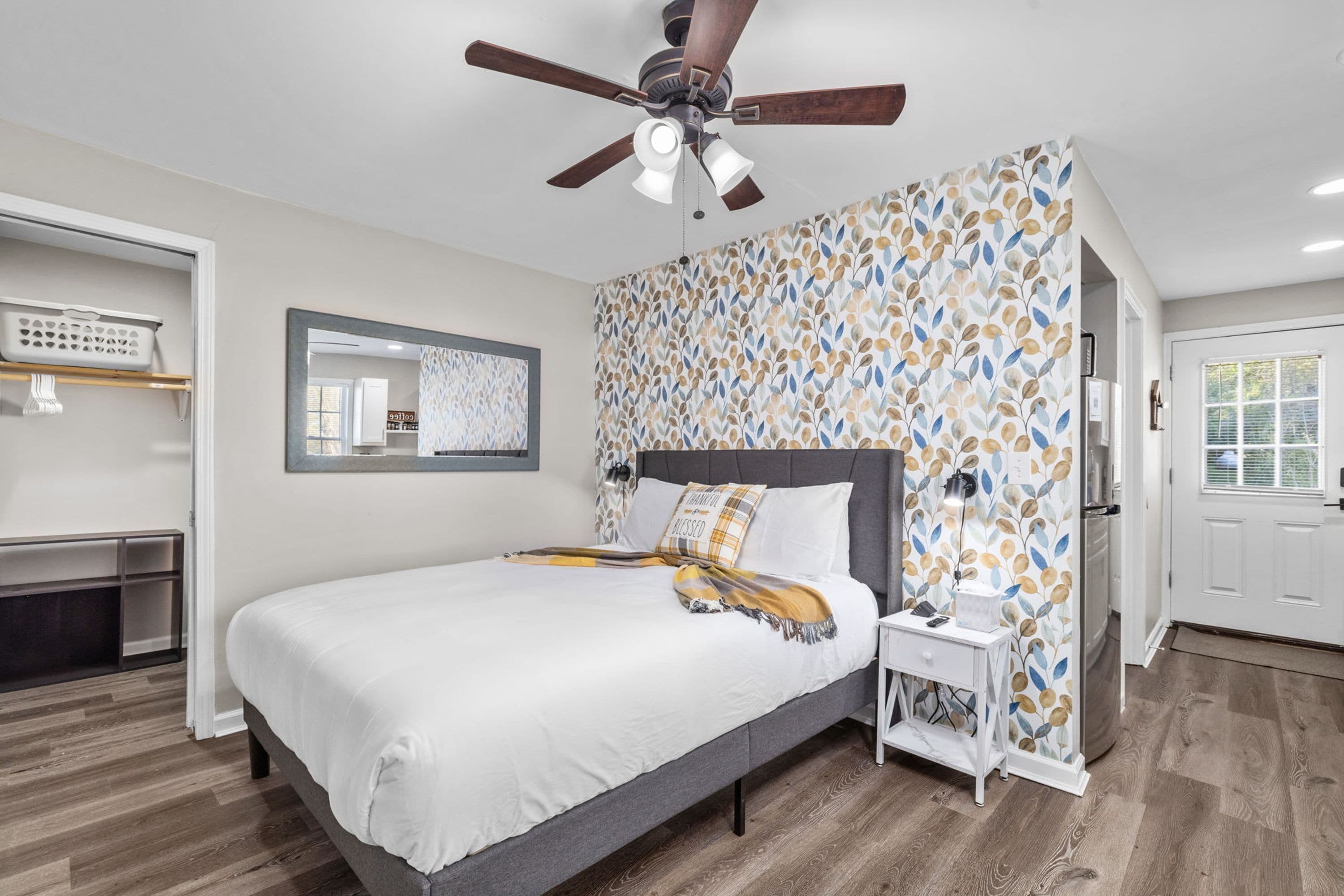 Une chambre à coucher avec un lit, une table de chevet, un ventilateur de plafond, un miroir et un mur décoré de motifs.