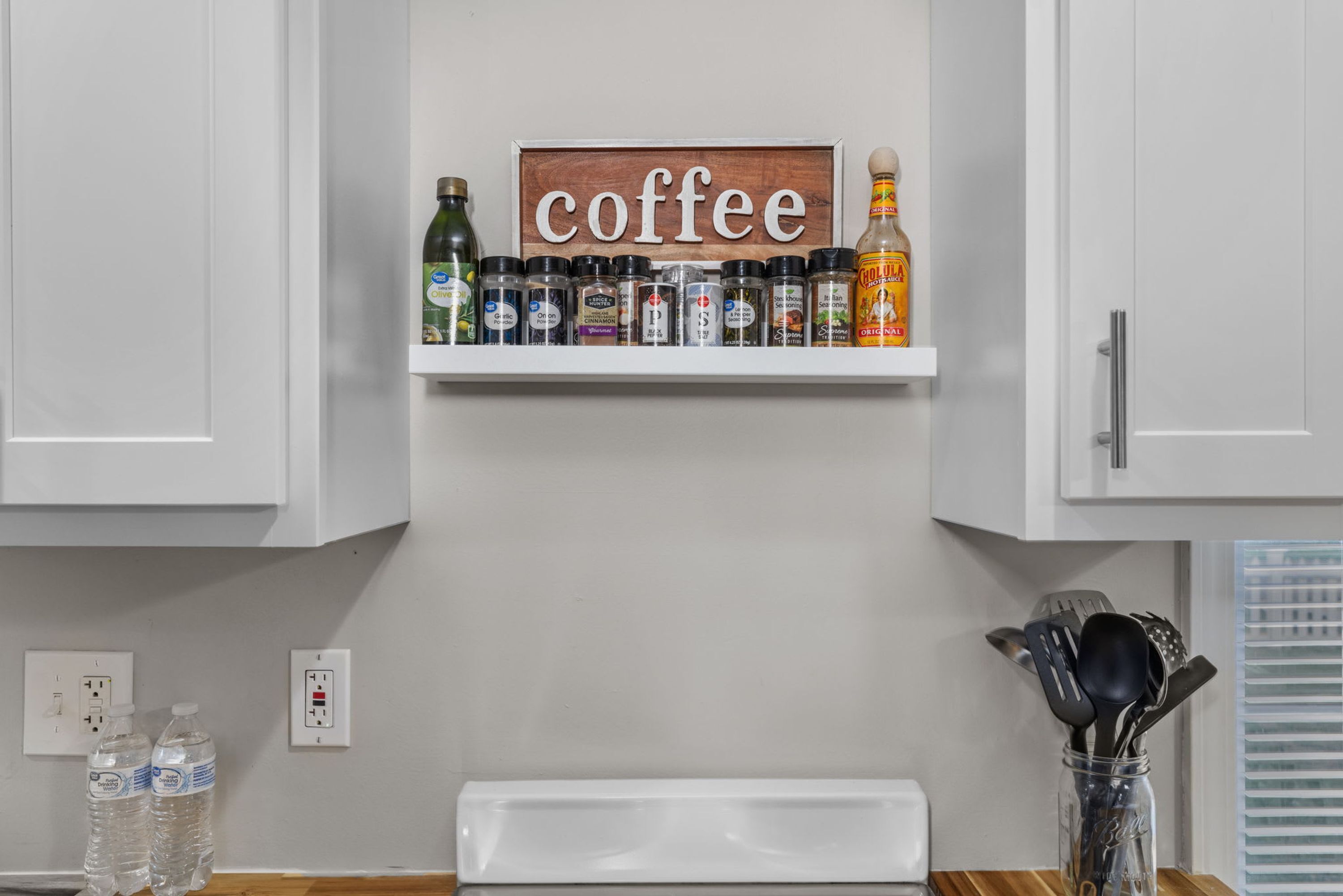 A kitchen with a shelf displaying various condiments and a sign that reads 'coffee'.