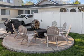 Een terras met vier Adirondack-stoelen, een vuurkorf en een overdekte barbecue.