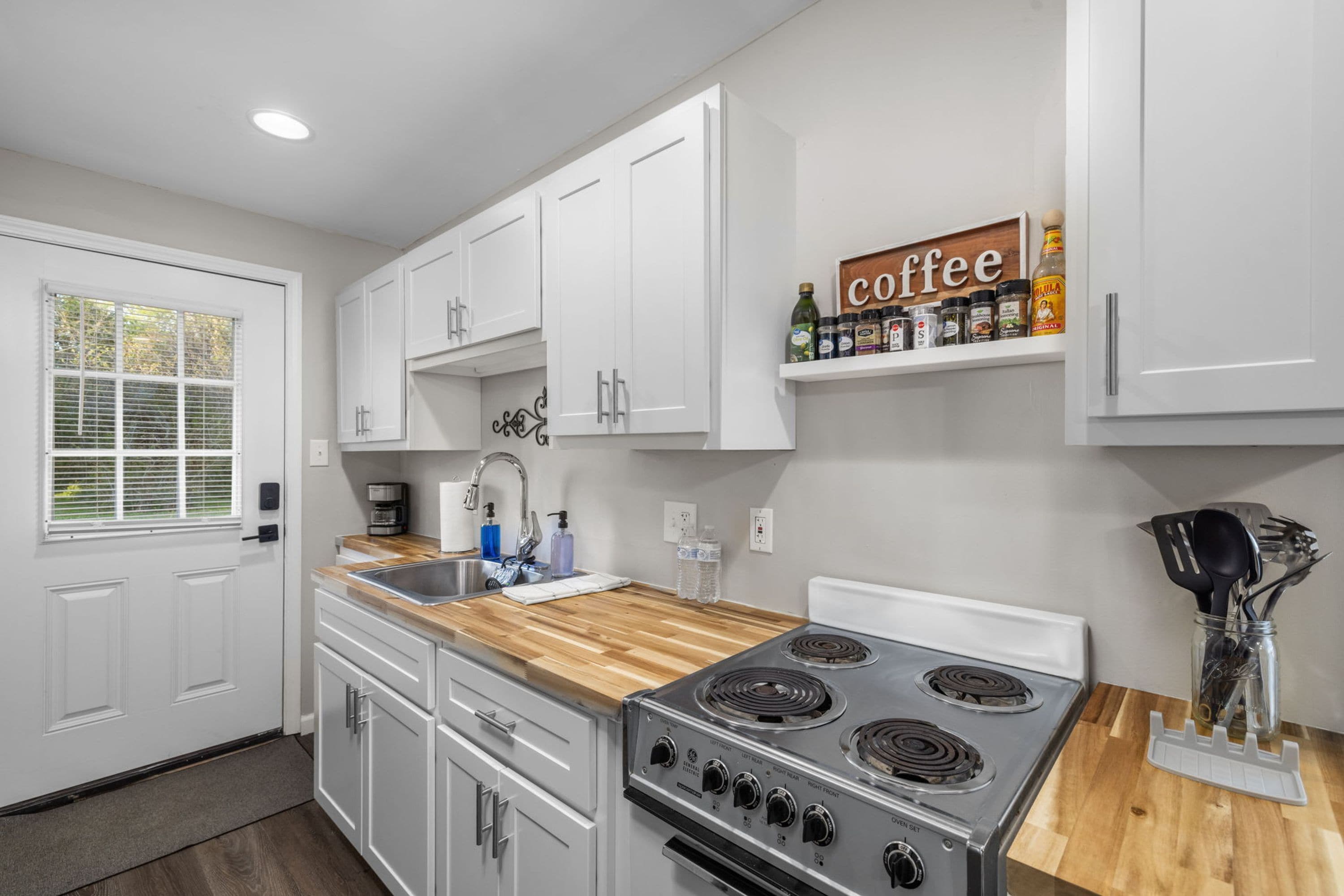 A kitchen with white cabinets, a stove, and a coffee shelf.