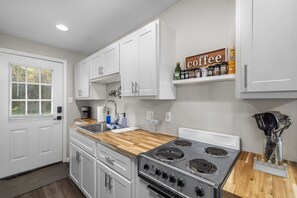 A kitchen with white cabinets, a stove, and a coffee shelf. - Downtown Kimmswick Studio Newly Renovated (Imperial)