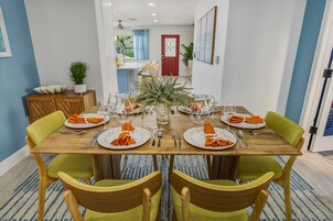 Uma sala de jantar com uma mesa de madeira posta para seis pessoas, rodeada por cadeiras verdes.