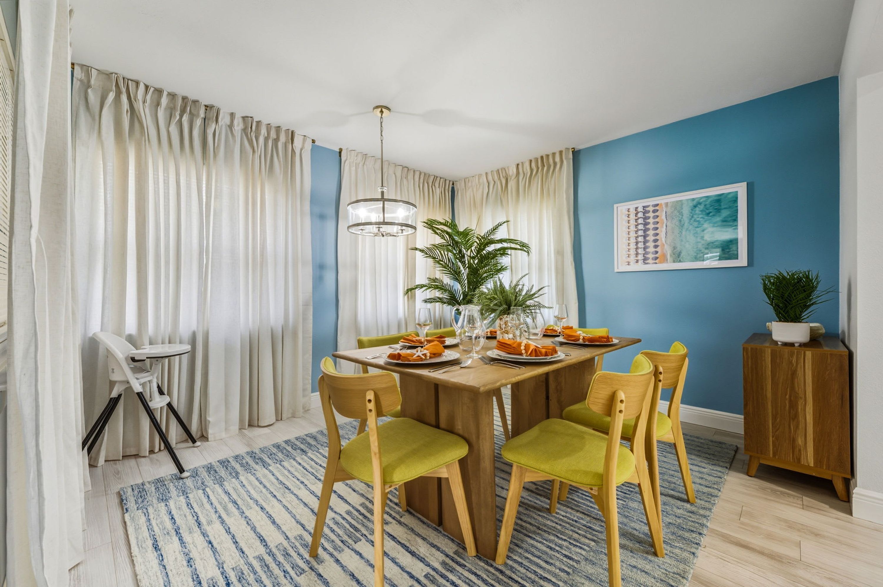 A dining area with a wooden table, green chairs, a chandelier, and a blue wall with a framed picture.