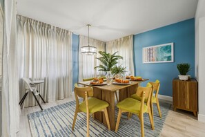 Ein Essbereich mit einem Holztisch, grünen Stühlen, einer Kandelaber und einer blauen Wand mit einem gerahmten Bild.