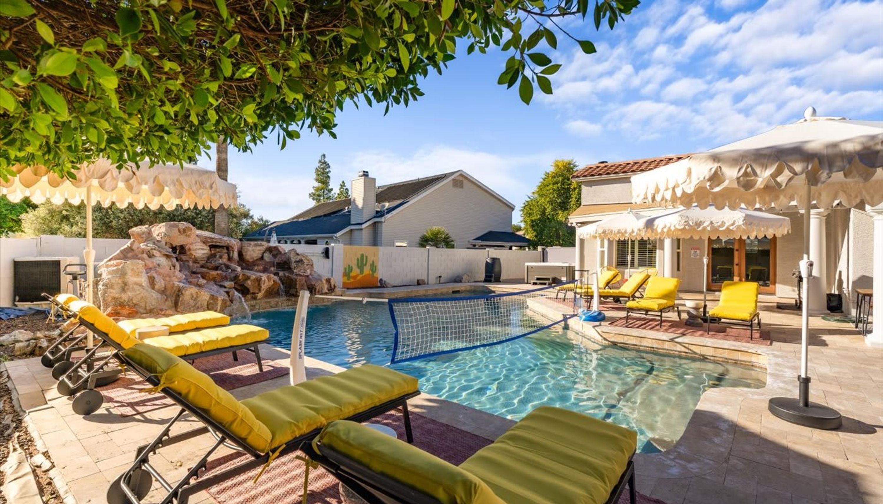A swimming pool with lounge chairs, a rock feature, and a house in the background.