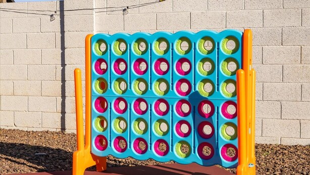 Een kleurrijk spelbord met een raster van gaten, geplaatst op een bakstenen muur.