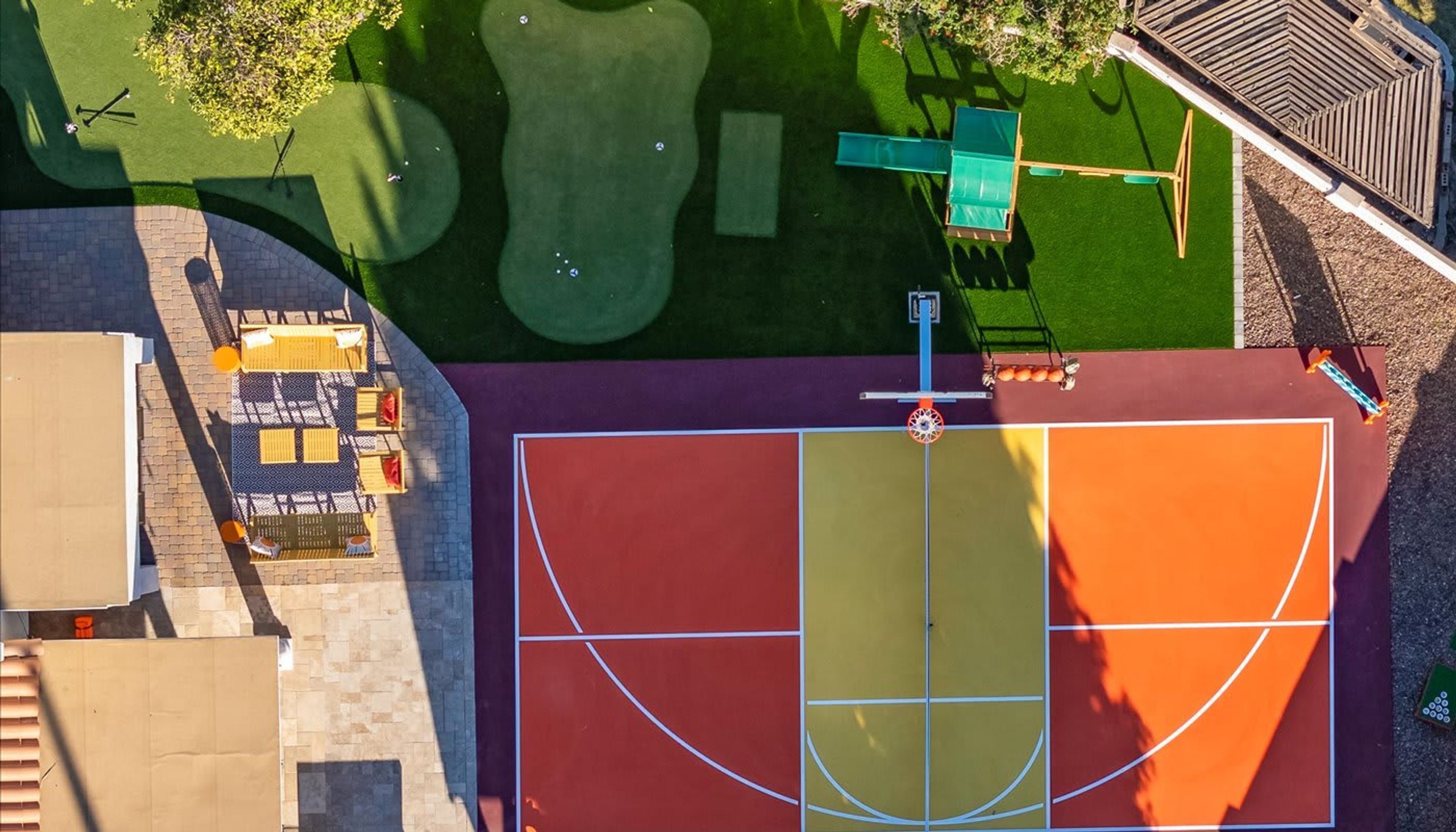 Vista aérea de una cancha deportiva con aro de baloncesto, junto a un área de descanso con mesas y sillas.