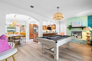 A modern living space with a pool table, wooden flooring, and a kitchen area with a stone backsplash. - Playcation Putt Putt Pool Tiki Bar Game Room (Largo)