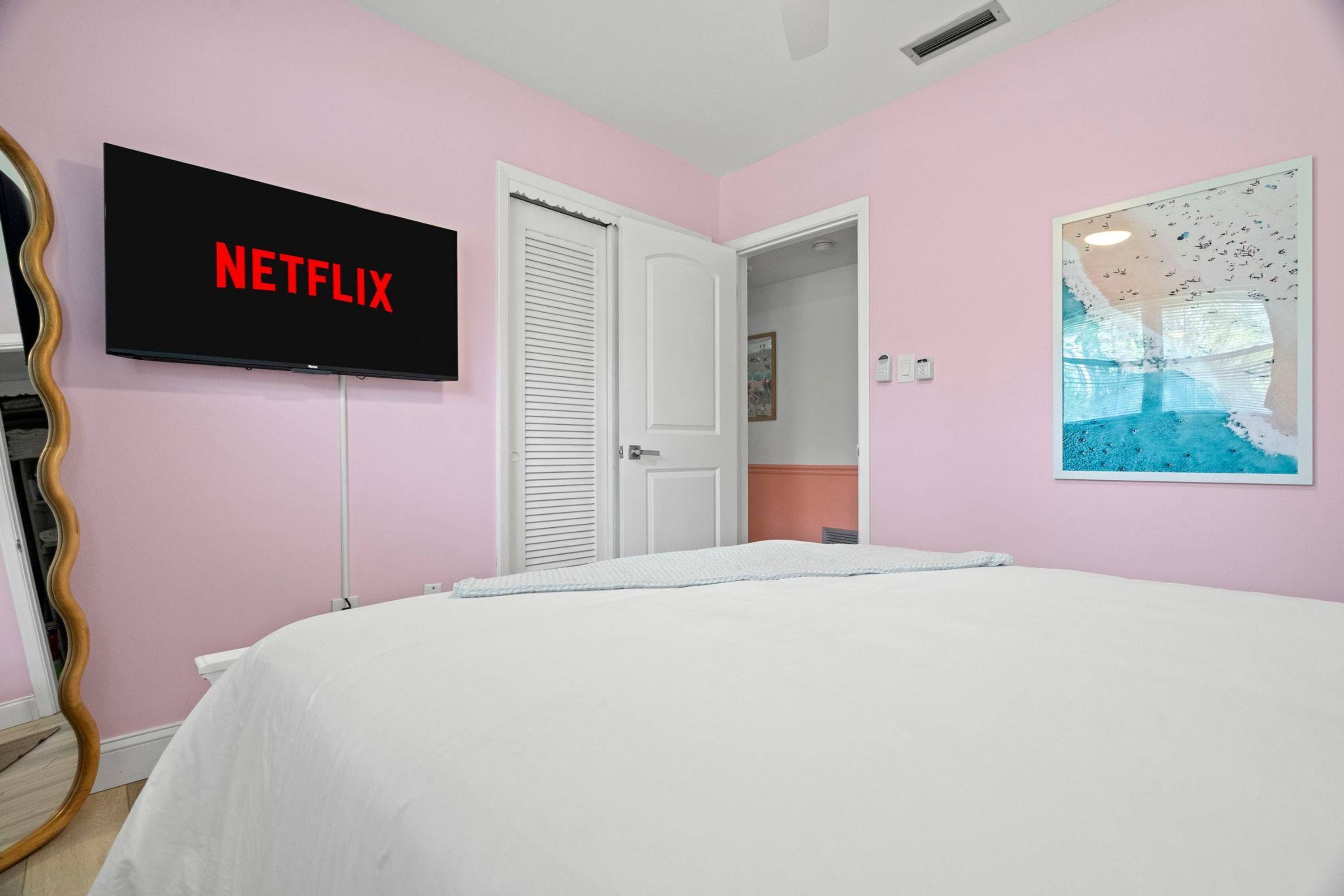 A bedroom with a bed, a television mounted on the wall displaying 'NETFLIX', a door, and a painting.