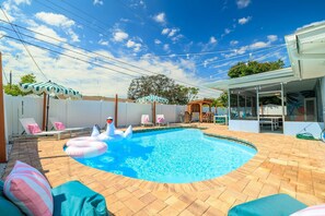 A backyard with a swimming pool, lounge chairs, and a covered patio area. - Playcation Putt Putt Pool Tiki Bar Game Room (Largo)