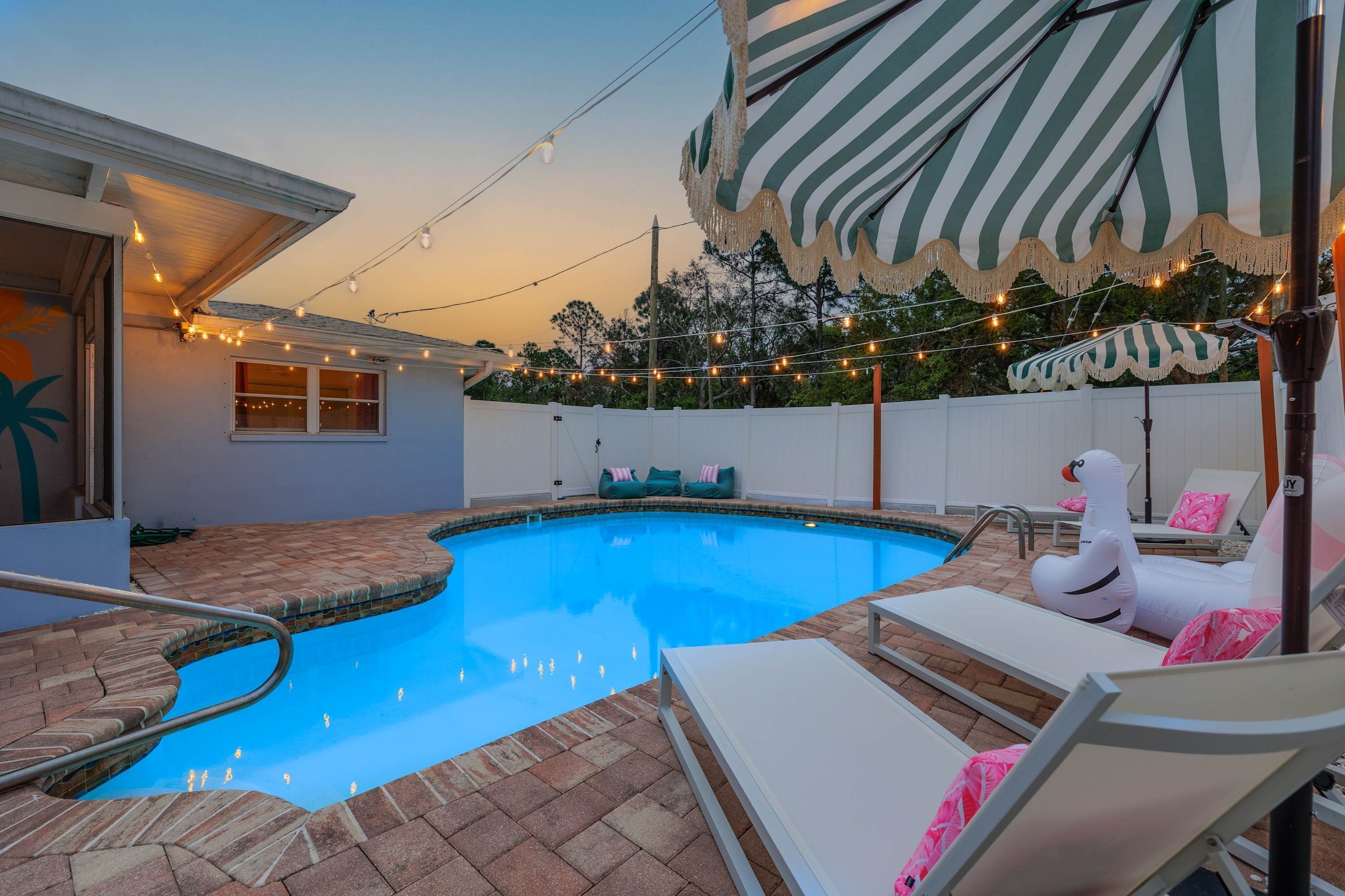 A swimming pool with a brick deck, lounge chairs, and string lights.