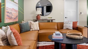 A living room with a brown leather sectional sofa, a round coffee table, and a large mirror on the wall. - The Ridge Family Pickleball Pool Hot Tub (Phoenix)