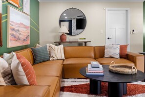 Ein Wohnzimmer mit einem braunen Ledersofa, einem runden Couchtisch und einem großen Spiegel an der Wand.
