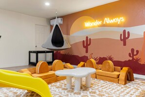 A children's play area with a slide, cushioned seating, and a wall mural. - The Ridge Family Pickleball Pool Hot Tub (Phoenix)