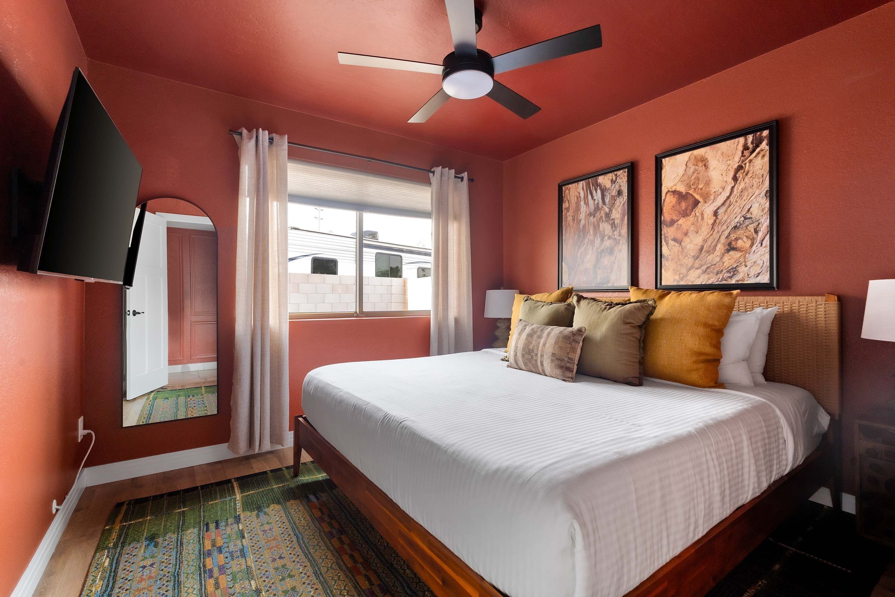 A bedroom with a bed, a ceiling fan, a window with curtains, and two framed pictures on the wall.