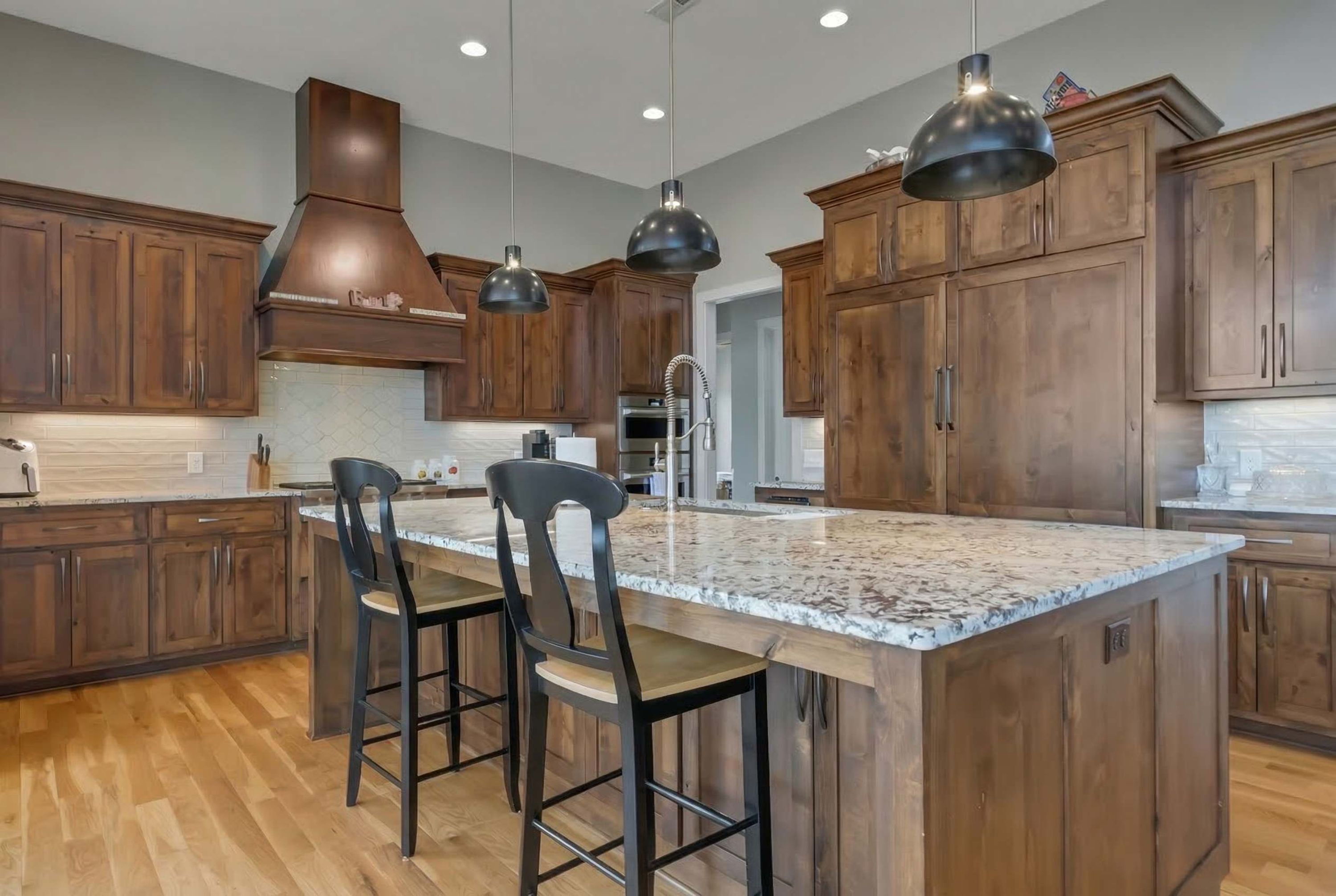 A modern kitchen with wooden cabinets, a large island with bar stools, and pendant lighting.